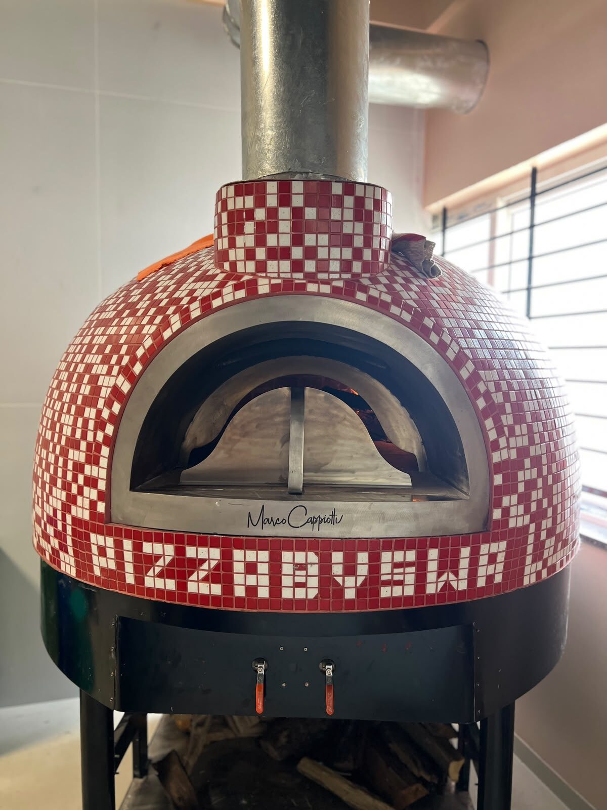 Our wood-fired oven at Pizza by Swa, tiled in a red and white mosaic, fire lit inside